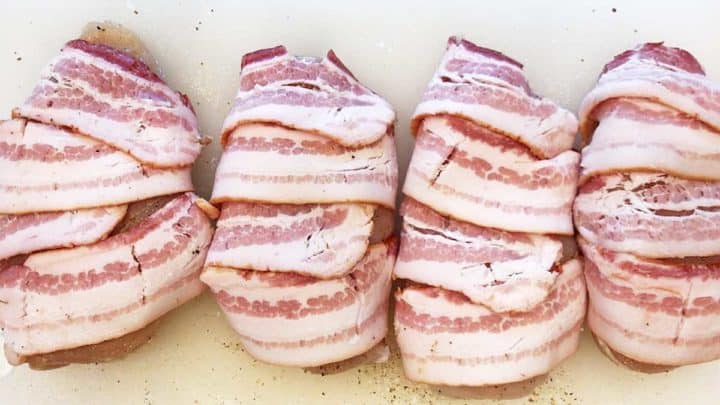 Raw chicken breasts wrapped in uncooked bacon.