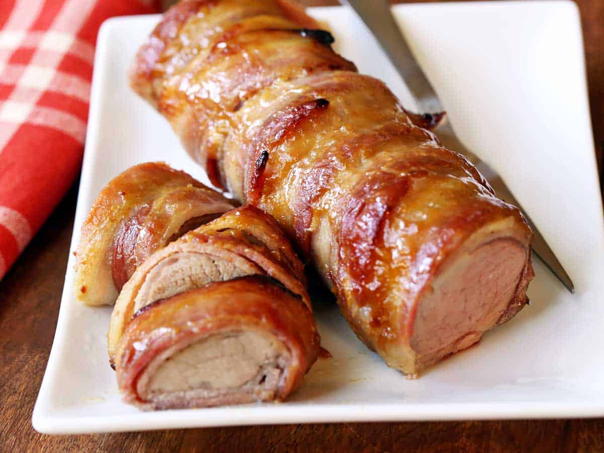 Pork tenderloin, wrapped in bacon and sliced, served on a white plate. 