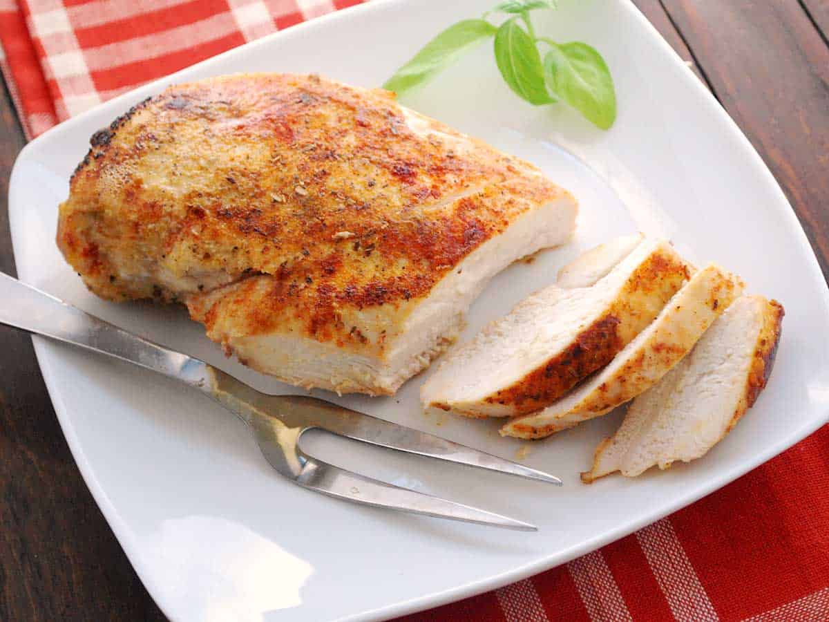 Sliced baked chicken breast served on a white plate with a serving fork. 