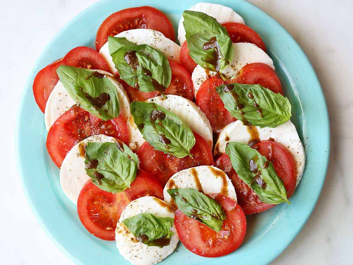 Caprese salad with tomatoes, mozzarella and basil, served on a green plate. 