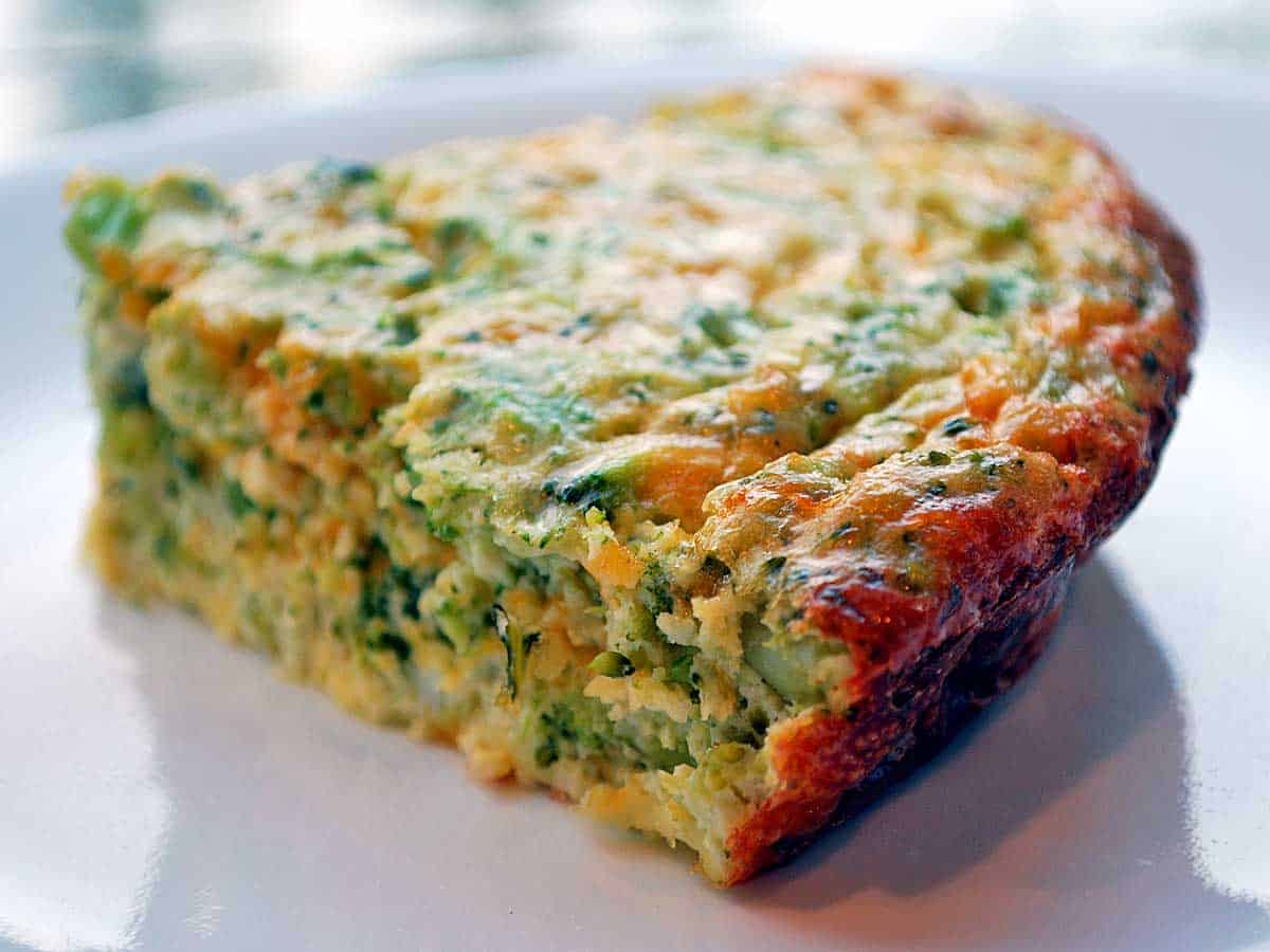 A slice of a crustless broccoli quiche served on a white plate.