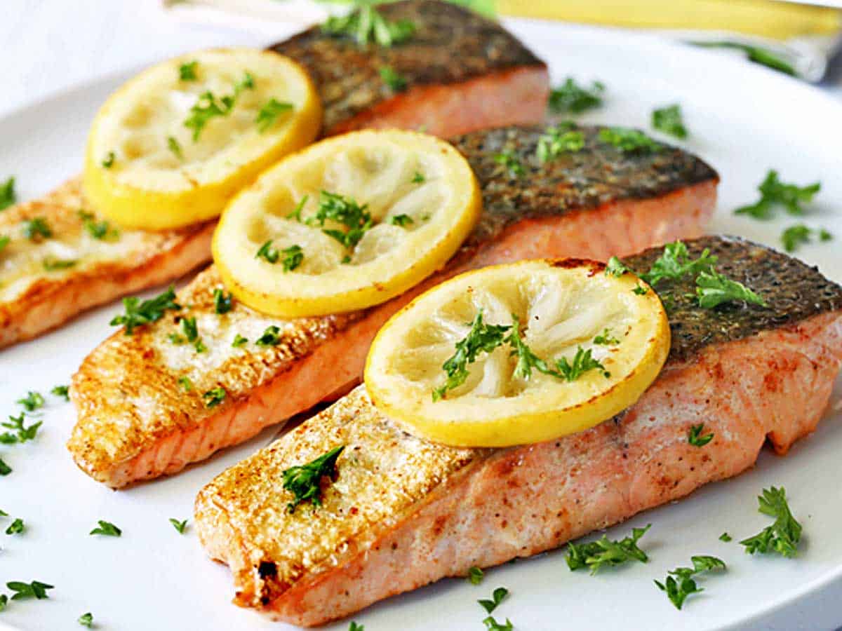 Pan-fried salmon served on a white plate, topped with lemon slices. 
