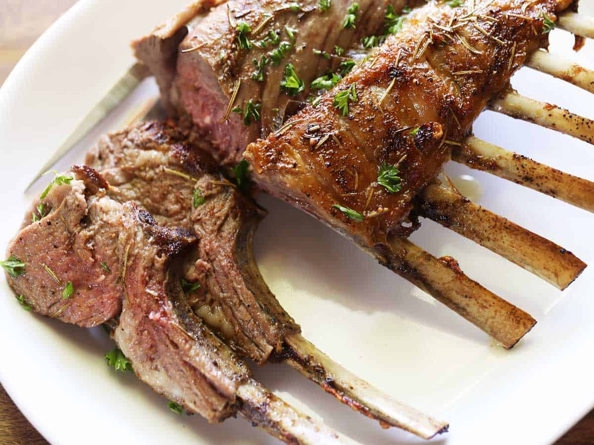 Roasted rack of lamb, sliced, served on a white plate. 