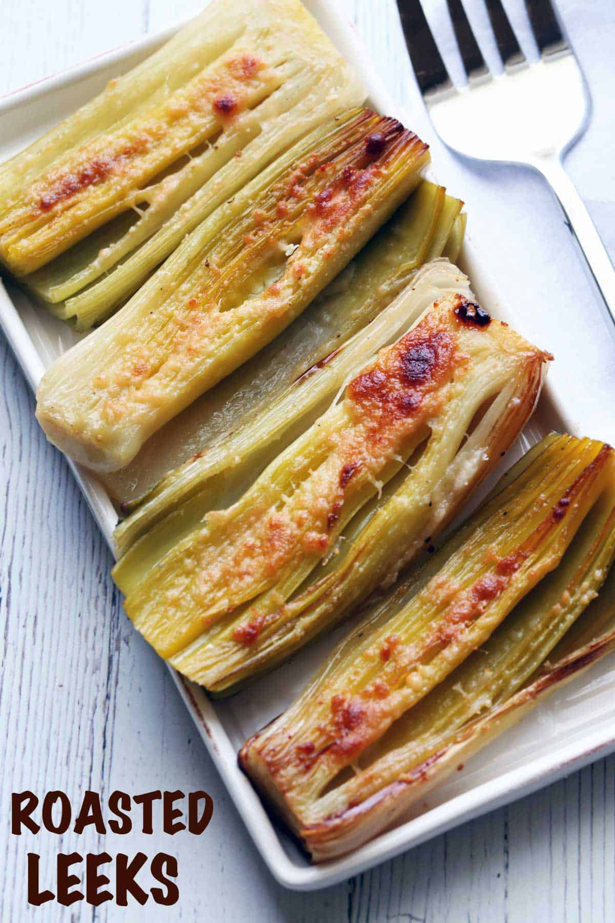 Roasted leeks served on a white tray with a serving fork. 
