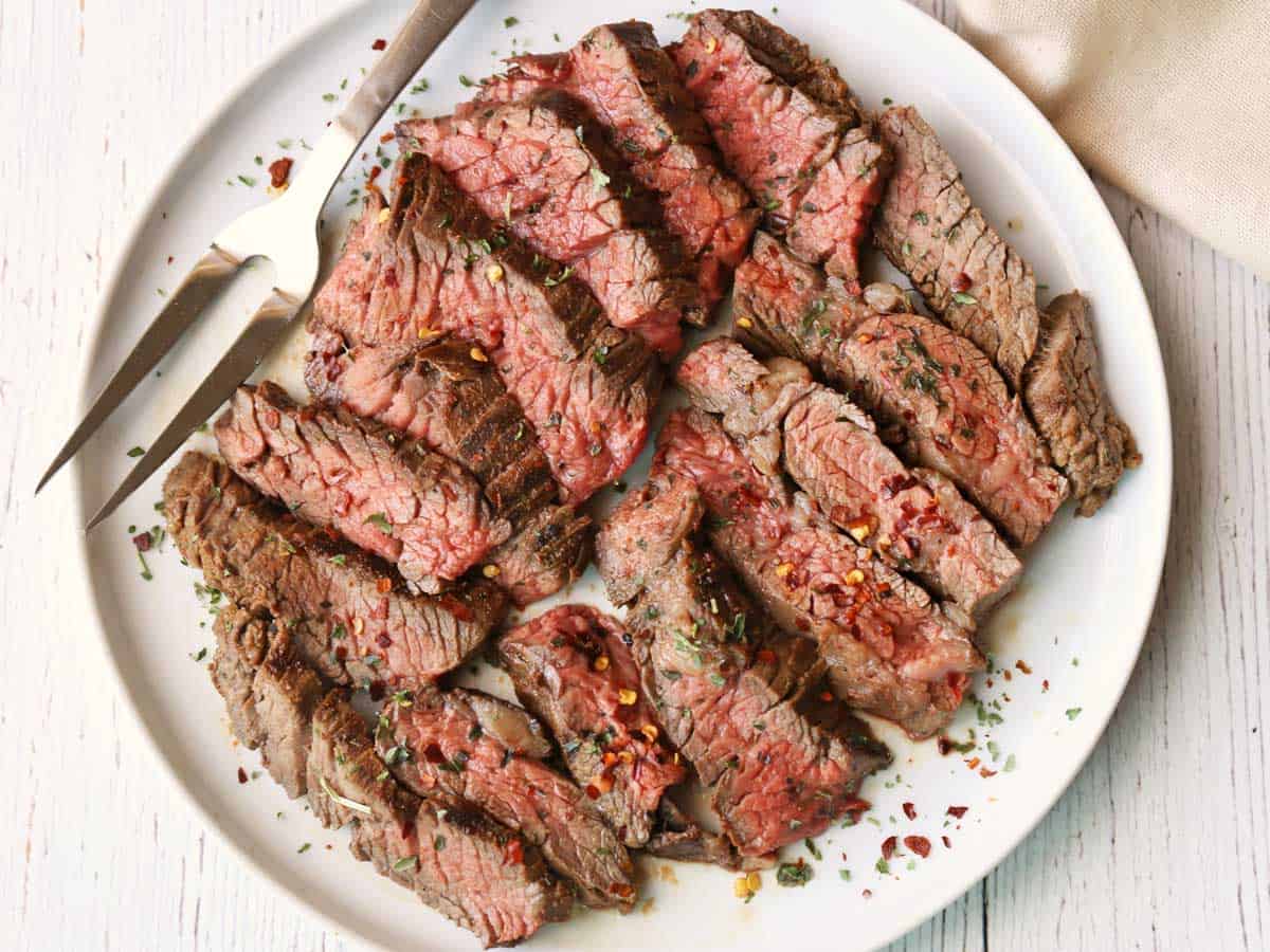 Slices of grilled skirt steak arranged on a white plate. 