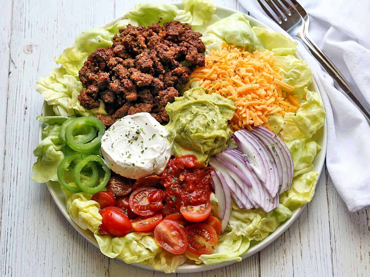 Taco salad served on a white plate with a napkin and two forks. 