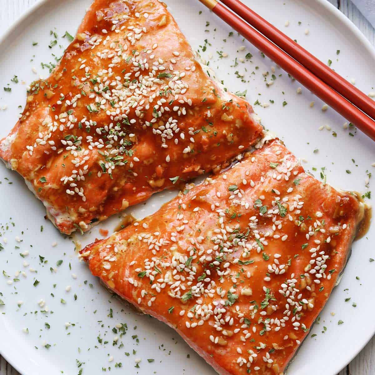 Teriyaki salmon served on a white plate with chopsticks.