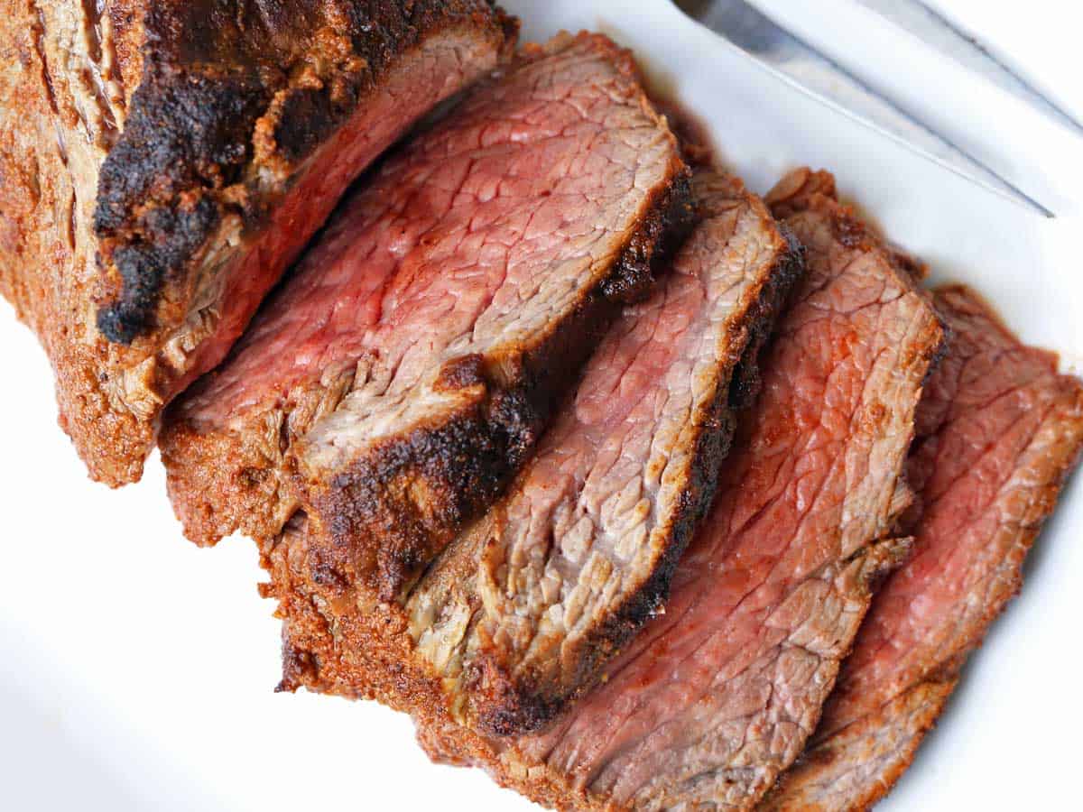 Sliced tri-tip roast served on a white plate with a serving fork. 