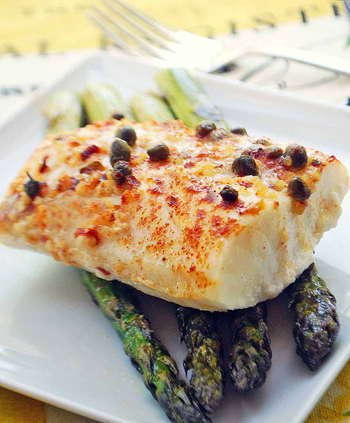 Baked cod served on a white plate with asparagus. 