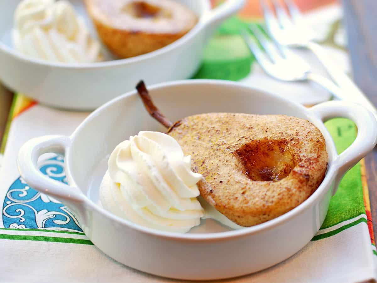 Baked pears served in a white dish with whipped cream.