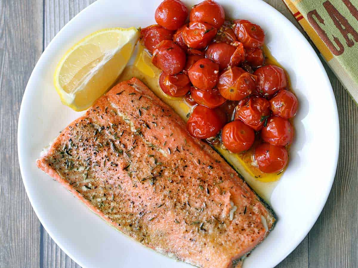 Broiled salmon served with tomatoes and a lemon wedge. 