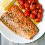 Broiled salmon served with tomatoes and lemon.