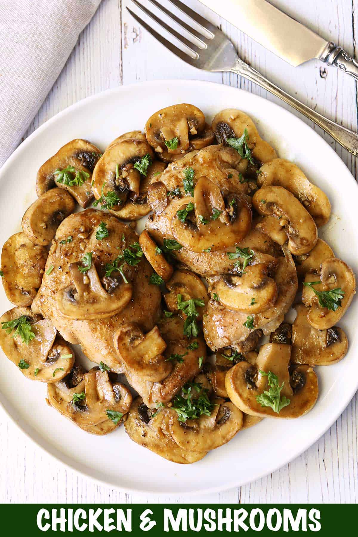 Chicken and mushrooms served on a white plate with utensils and a napkin. 