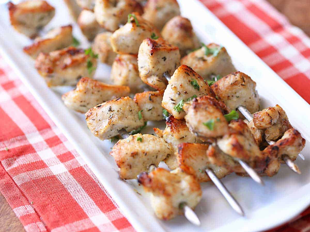 Oven-baked chicken kabobs served on a white tray with a red napkin. 