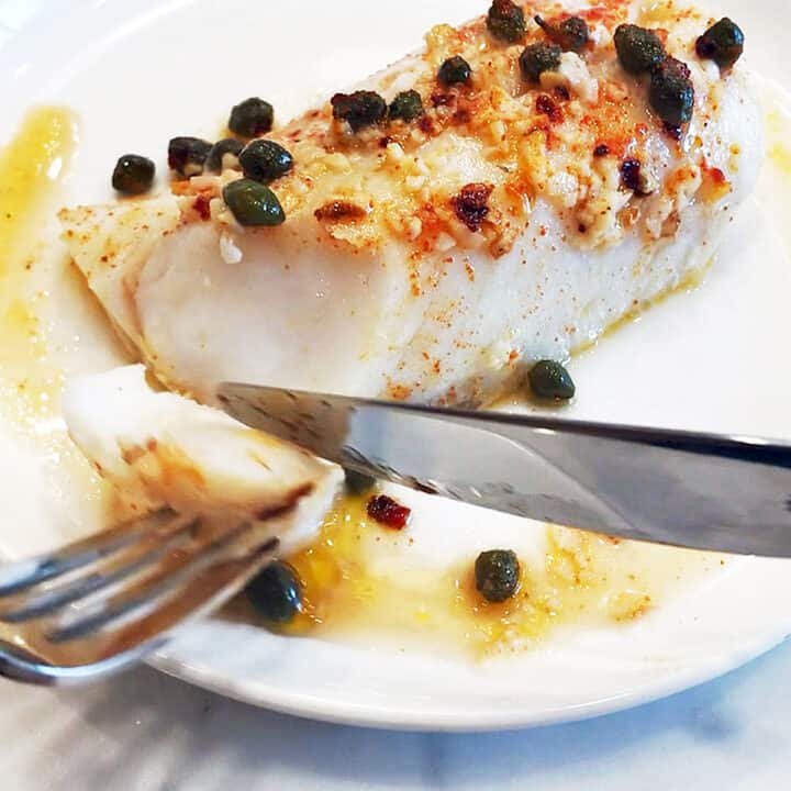 Baked cod flaked with a fork to show its flesh is white and opaque.