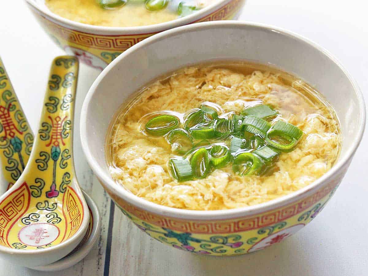 Two bowls of egg drop soup served with Chinese soup spoons. 
