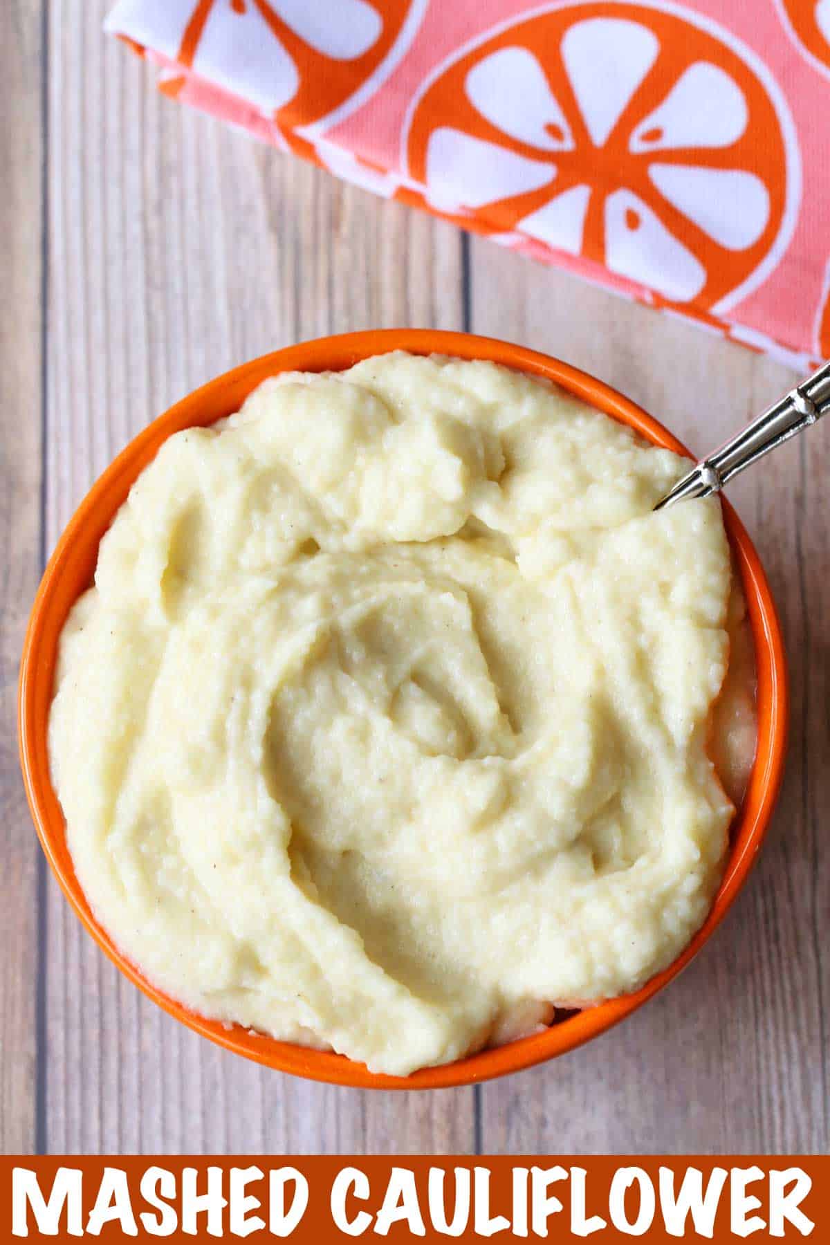 cauliflower mash served in an orange bowl with a serving spoon. 
