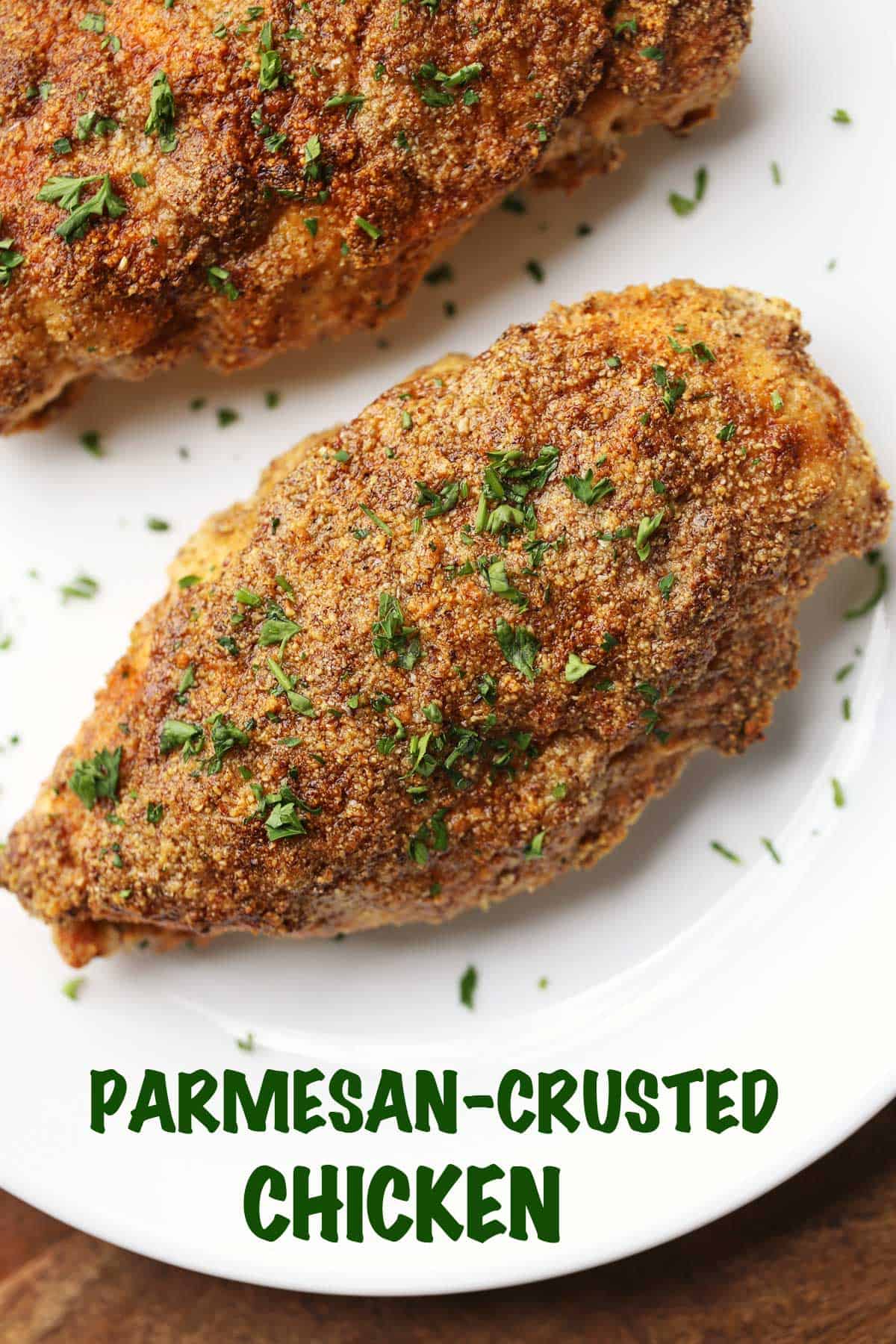 Two pieces of parmesan-crusted chicken topped with parsley and served on a white plate. 