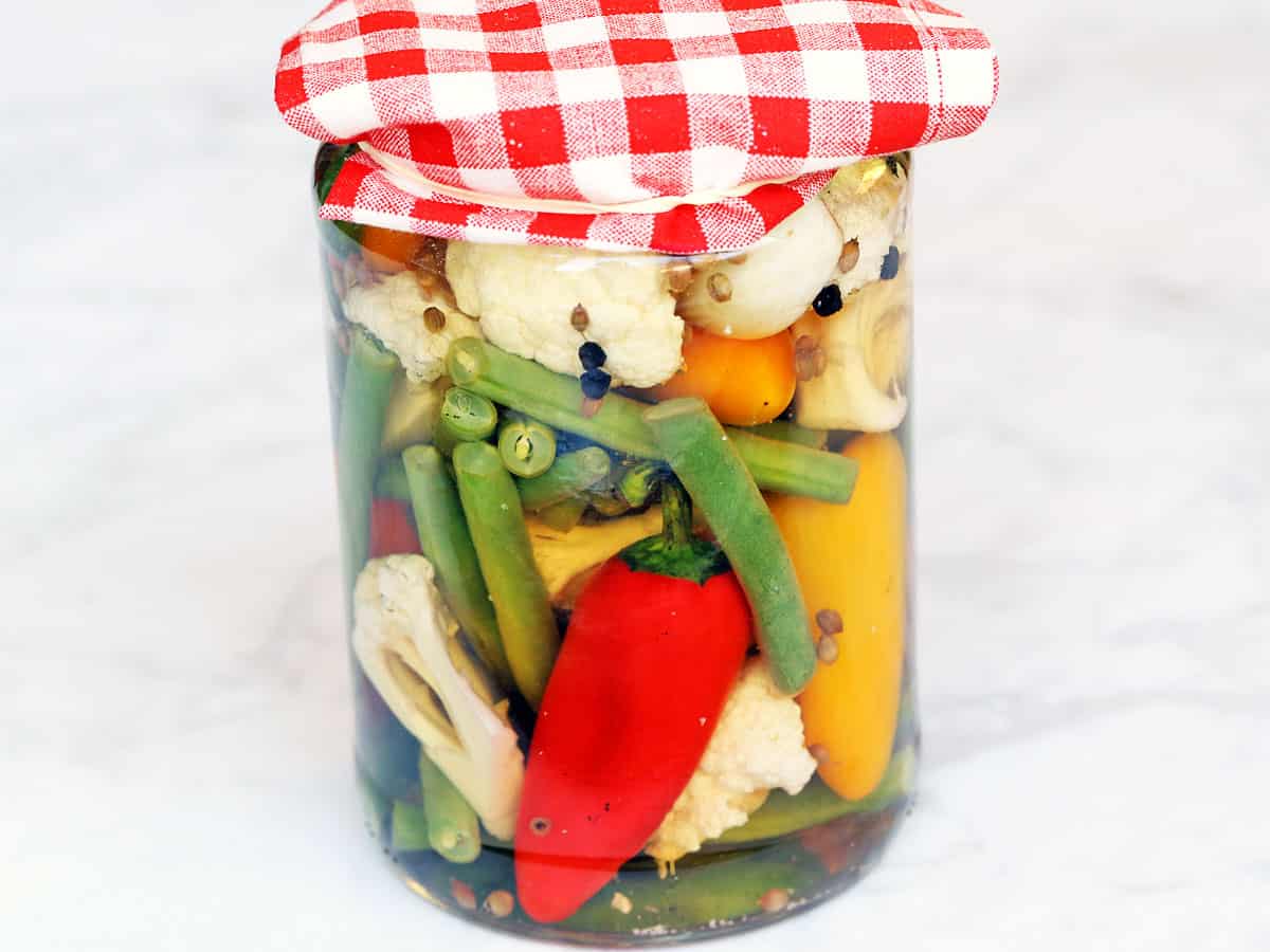 Quick pickles served in a glass jar with a red-and-white checkered napkin on the lid. 