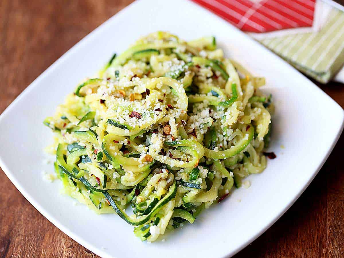 Zucchini noodles with butter and parmesan served on a white plate.
