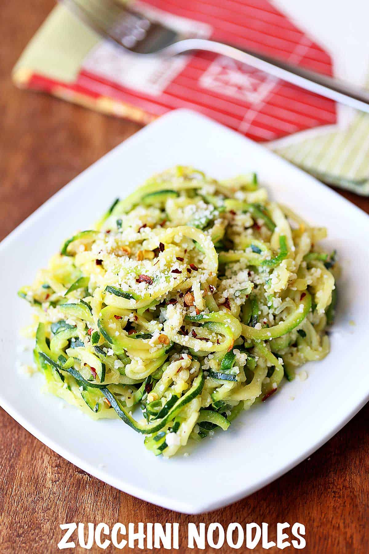 Buttered zucchini noodles served on a white plate with a napkin. 