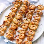 Grilled shrimp are threaded on skewers and served on a white plate.