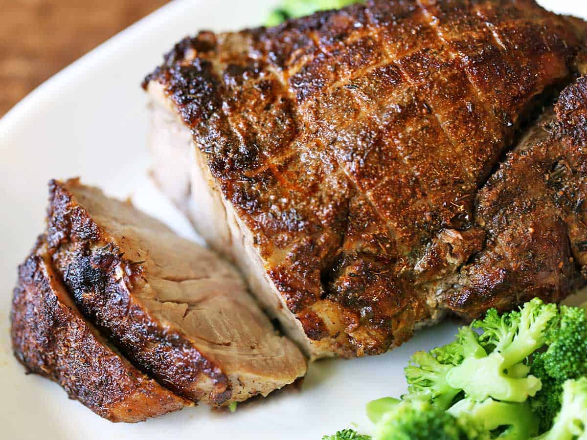 Pork roast is served with steamed broccoli. 