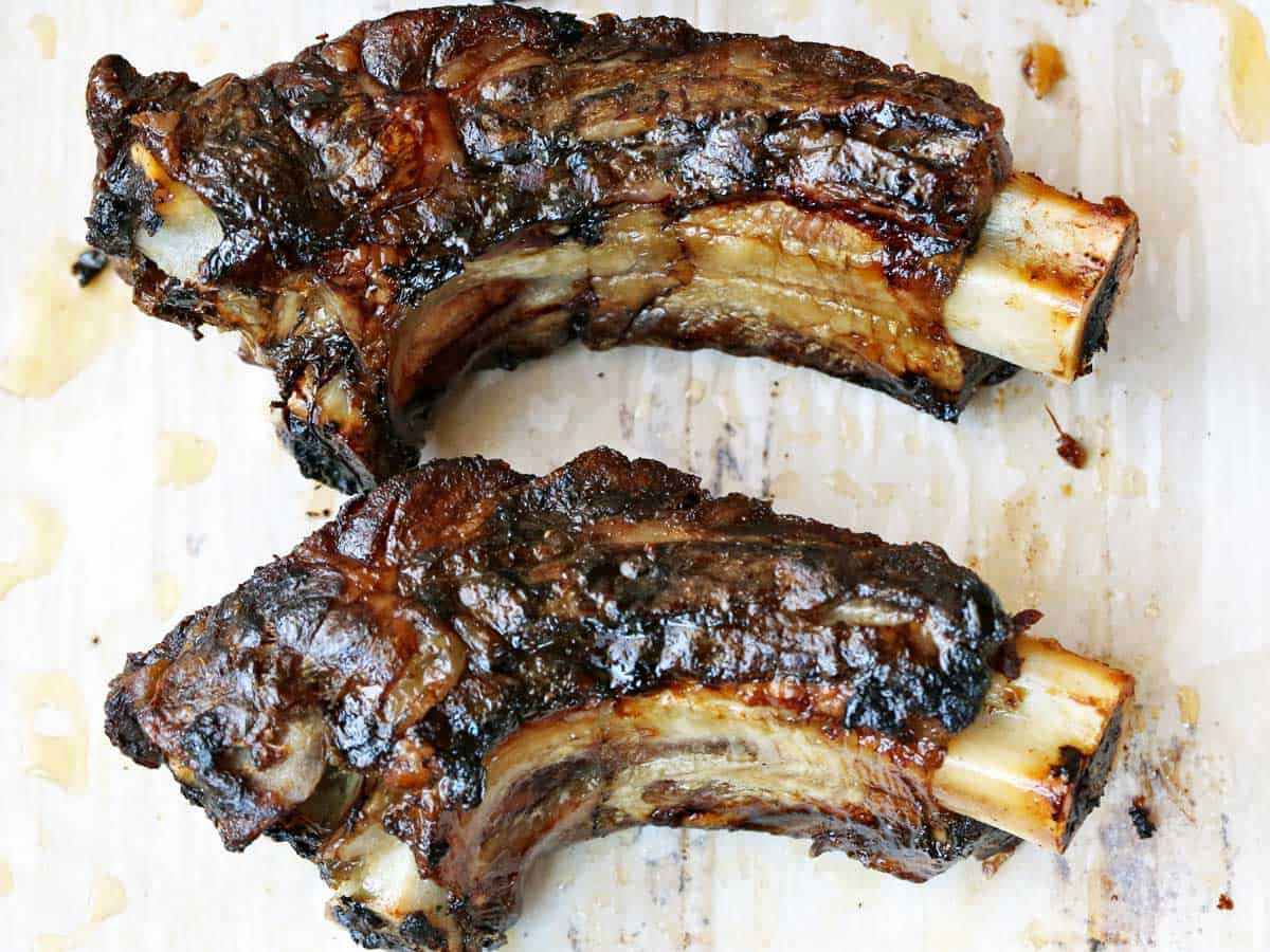 Two beef back ribs served on a parchment-lined baking sheet. 