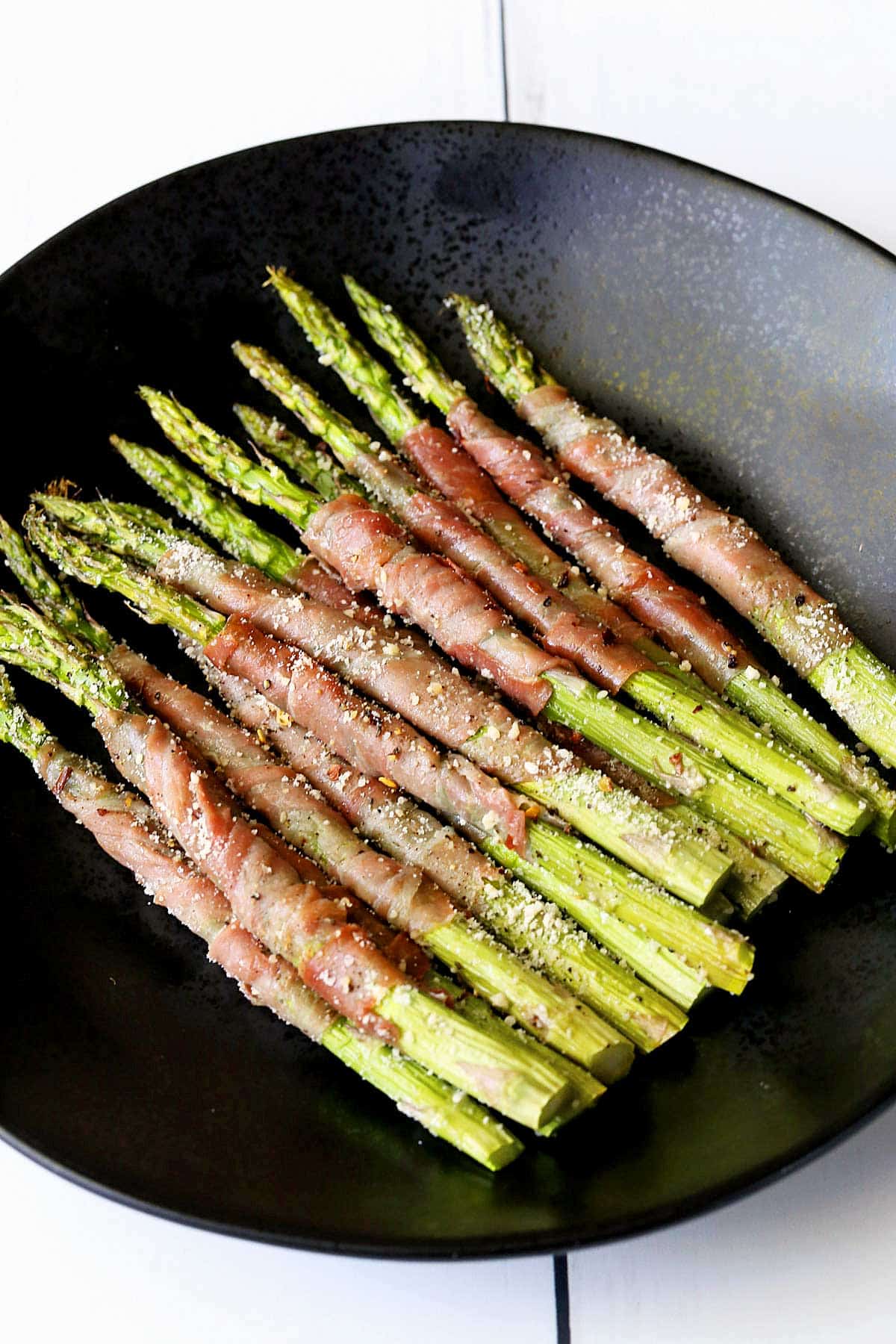 Prosciutto-wrapped asparagus served on a black plate. 