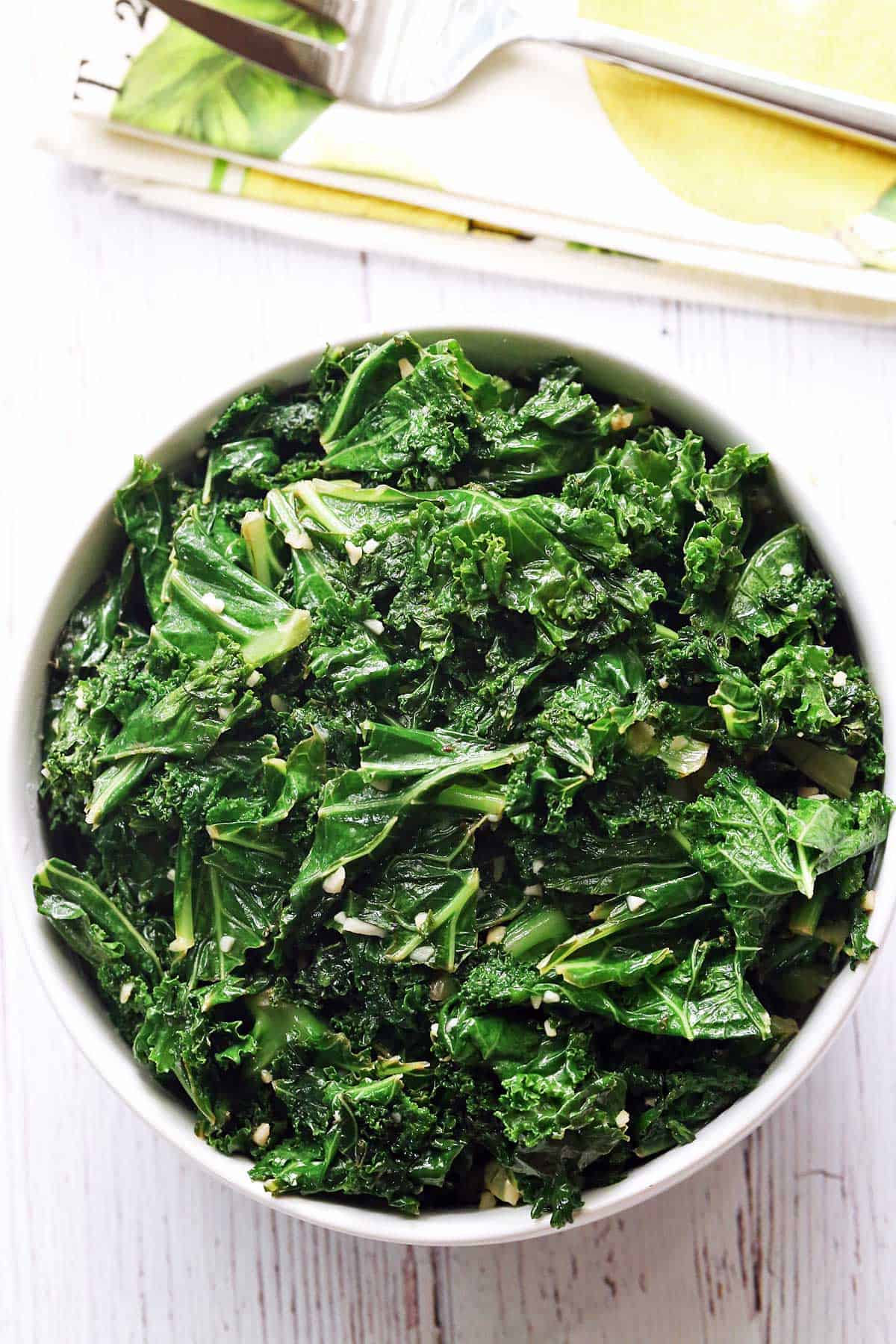 Sauteed kale served in a white bowl with a napkin and a fork. 