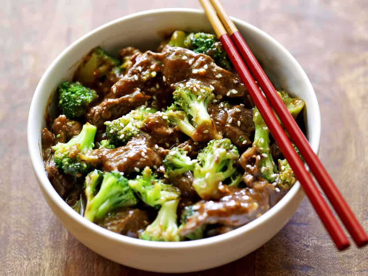 Beef and broccoli served in a white bowl with chopsticks. 