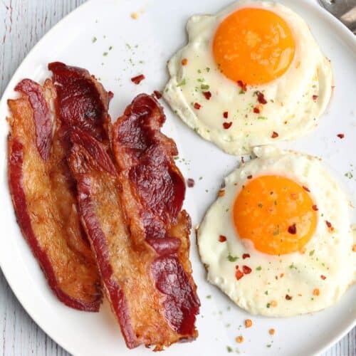 Beef bacon served with eggs on a white plate.