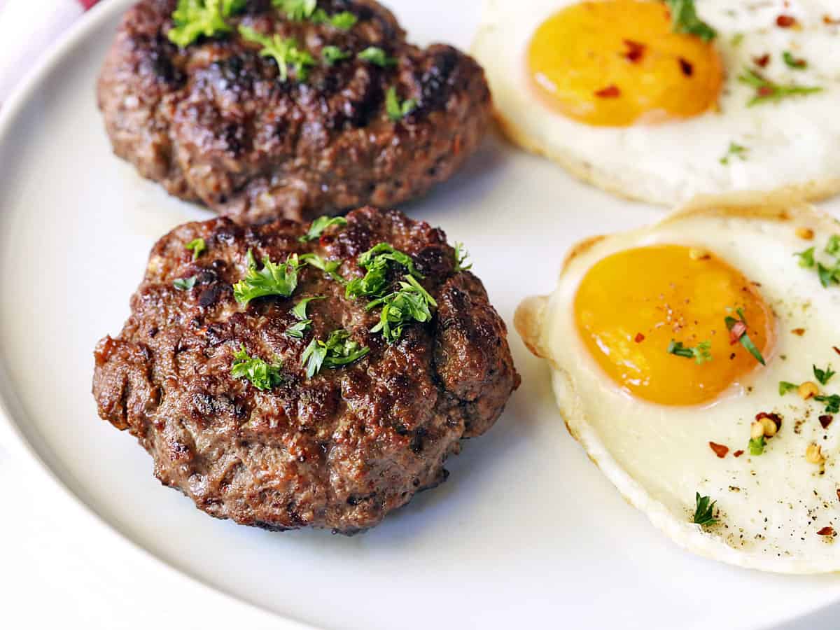 Beef sausage is served with fried eggs on a white plate.
