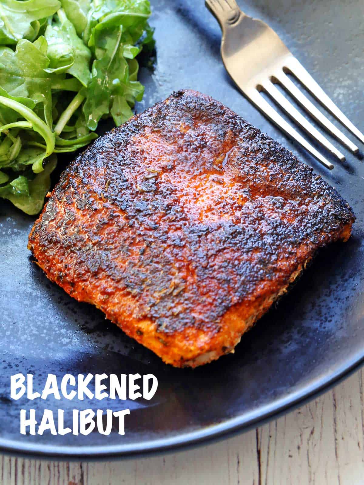 Blackened halibut served on a black plate with a side salad and a fork. 
