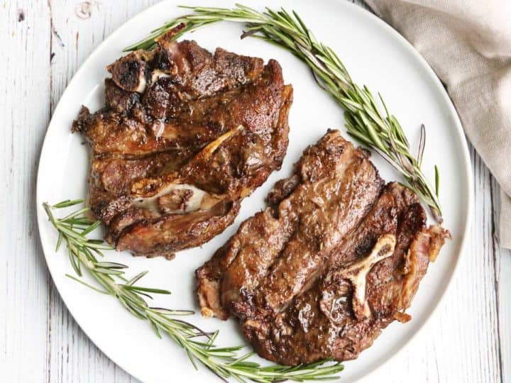 Two lamb shoulder chops served on a white plate, garnished with rosemary. 