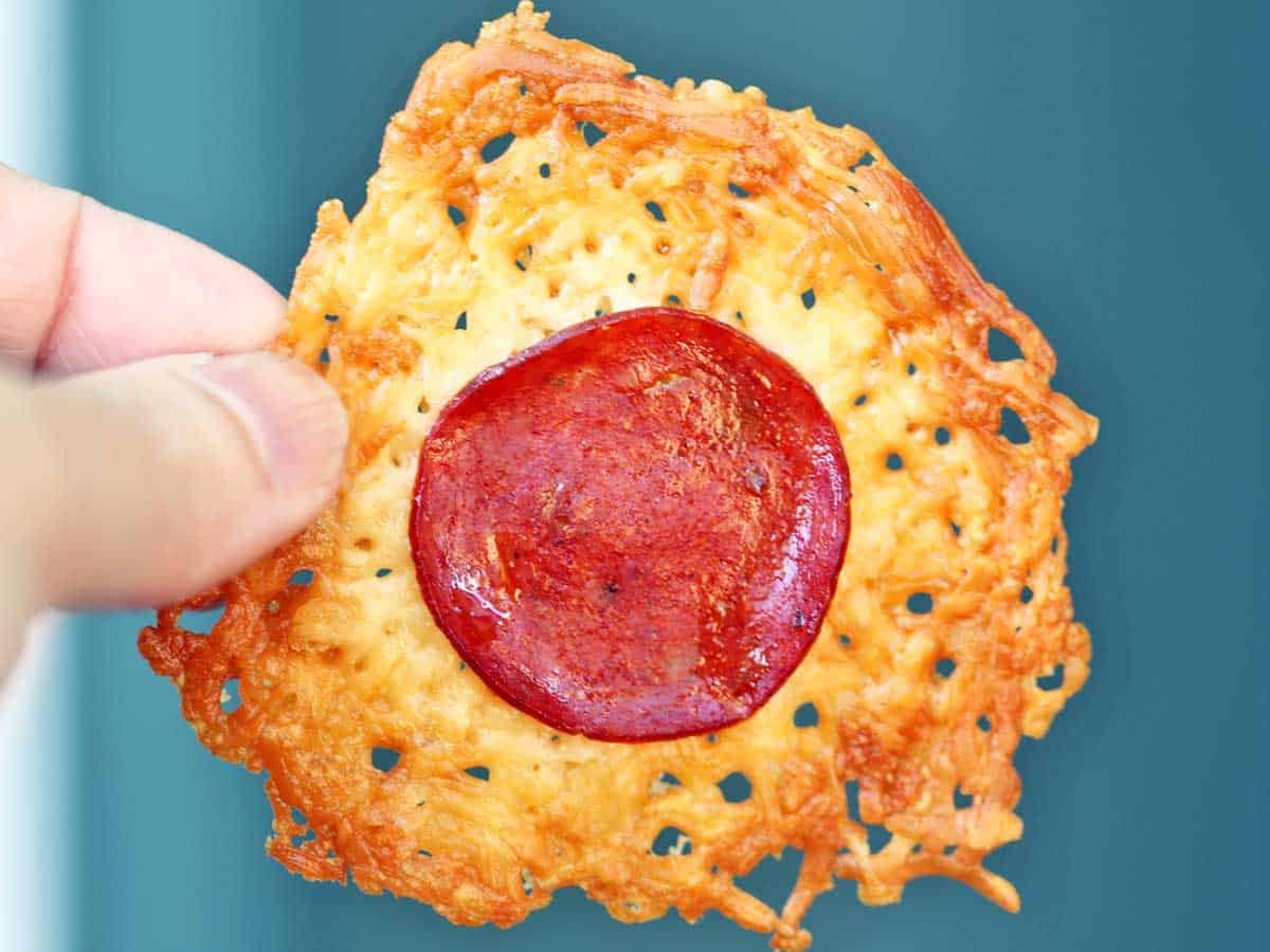 A parmesan crisp with pepperoni held in someone's hand. 