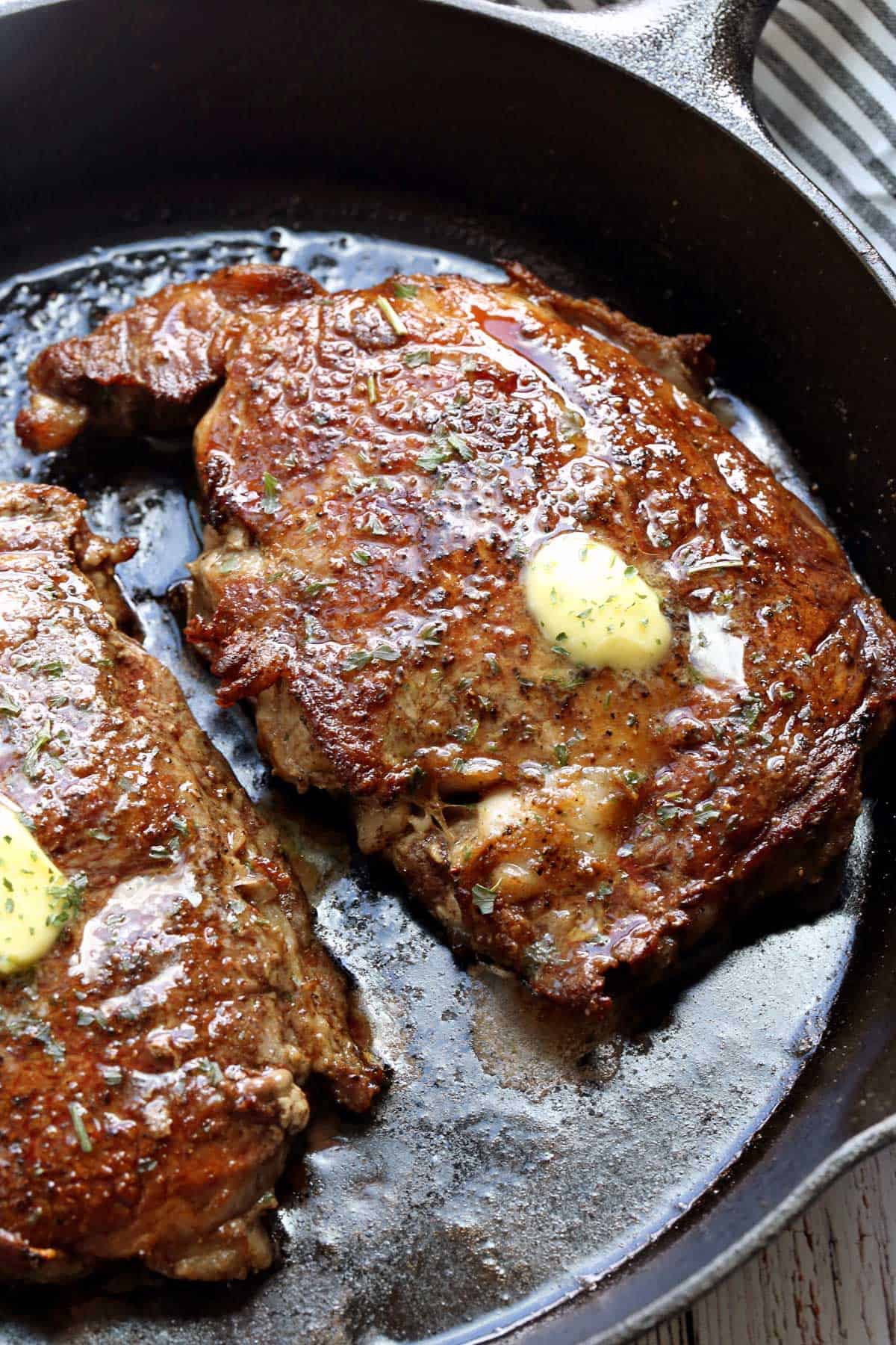 Two ribeye steaks topped with butter.