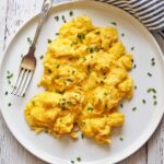 Fluffy scrambled eggs are served on a plate with a fork.
