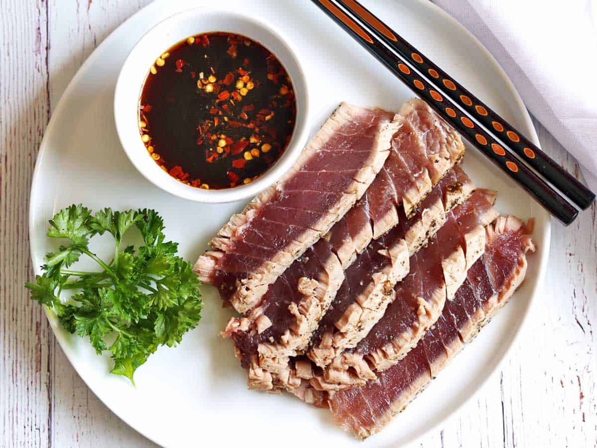 Slices of seared tuna served with a dipping sauce and chopsticks. 