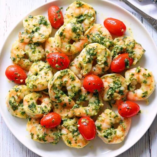 Pesto shrimp served with tomatoes on a white plate.
