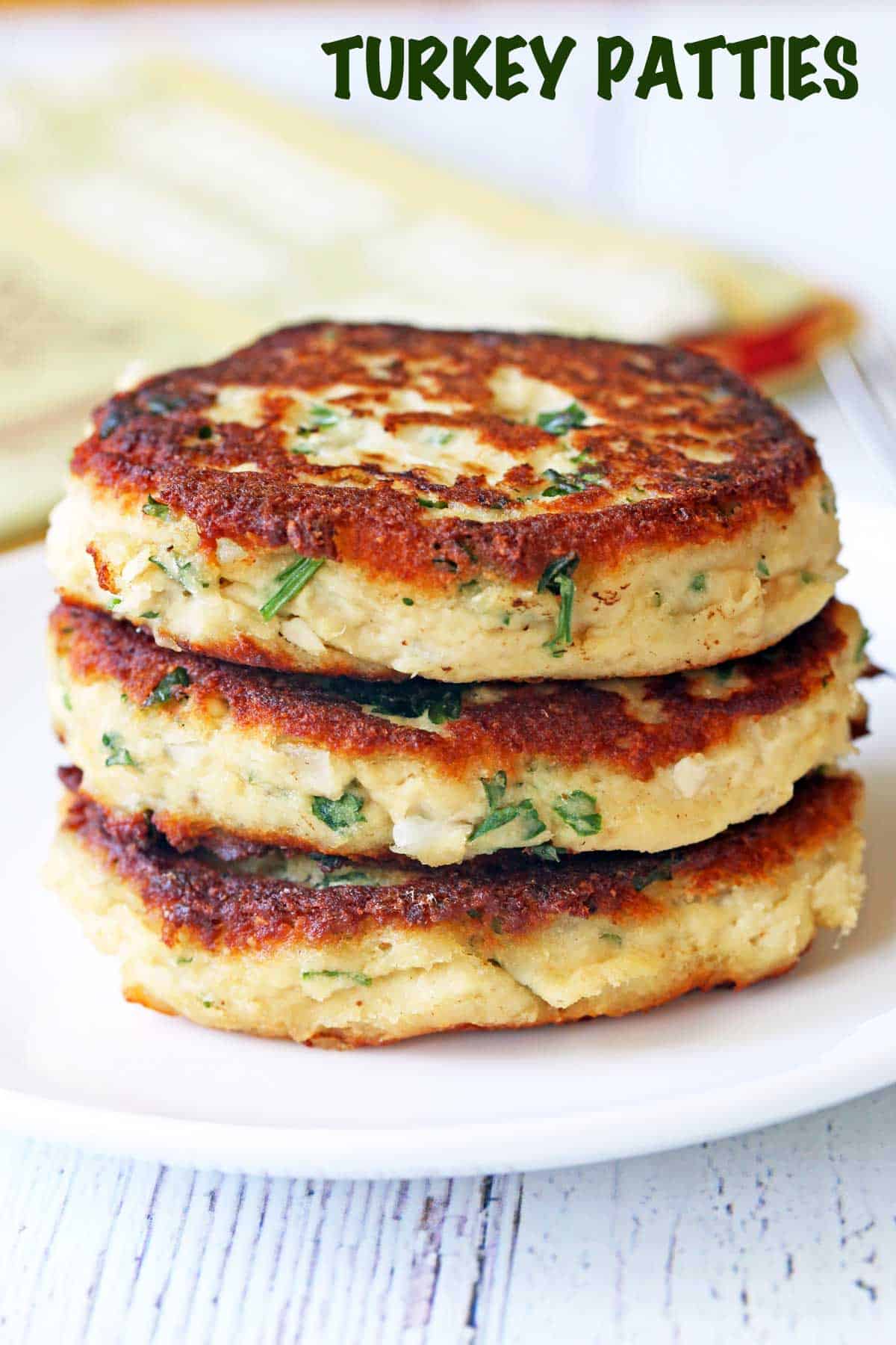 Three turkey patties stacked on a white plate. 