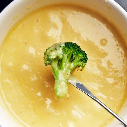 A broccoli piece is dipped into cheese fondue.