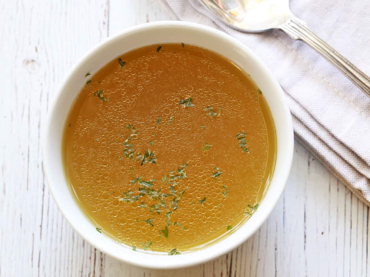 Homemade chicken broth served in a white bowl with a spoon. 