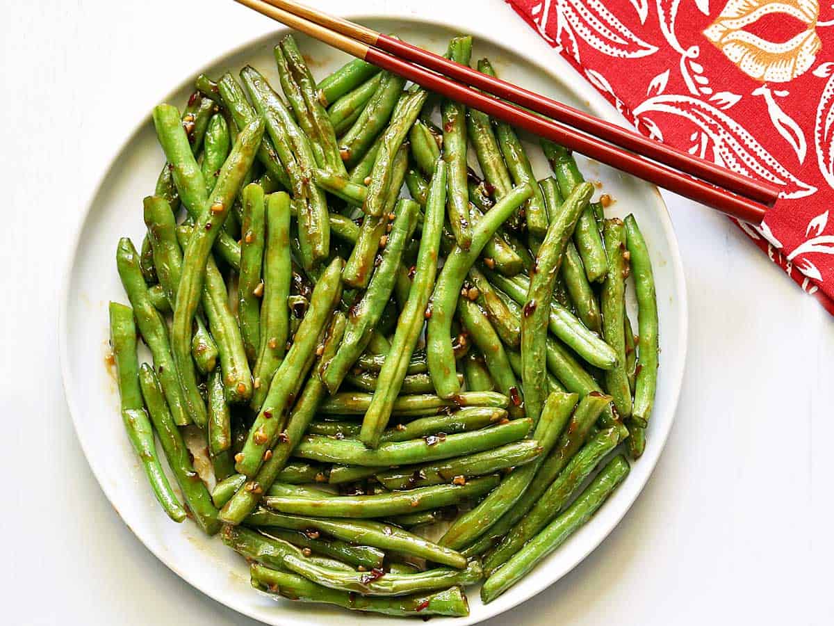 Chinese green beans served on a white plate with chopsticks. 