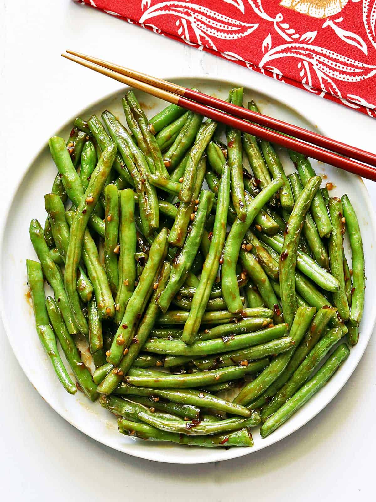 Chinese green beans served on a white plate with red chopsticks. 
