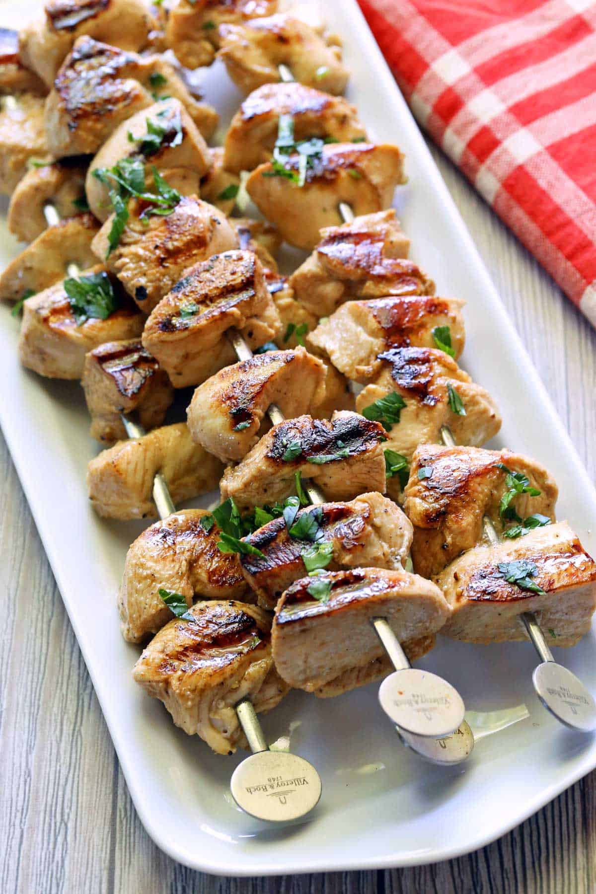 Grilled chicken skewers served on a white platter. 