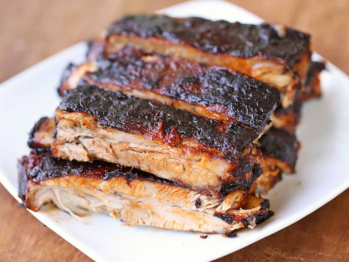 Oven-baked ribs piled on a white plate. 