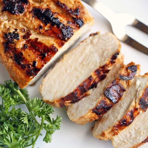 Grilled chicken breast, sliced and served on a white plate.