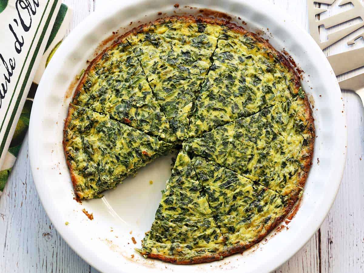 Crustless spinach quiche, sliced, is served in a white pie dish. 