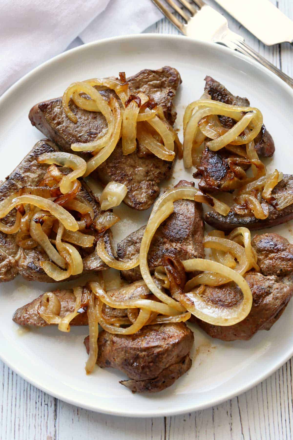 Beef liver and onions served on a white plate with a knife and a fork.